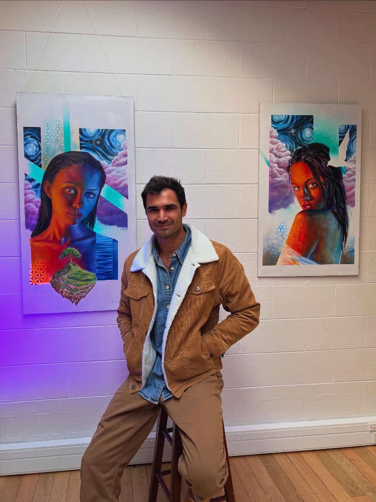 Artist seated in the studio between two large colorful portrait paintings