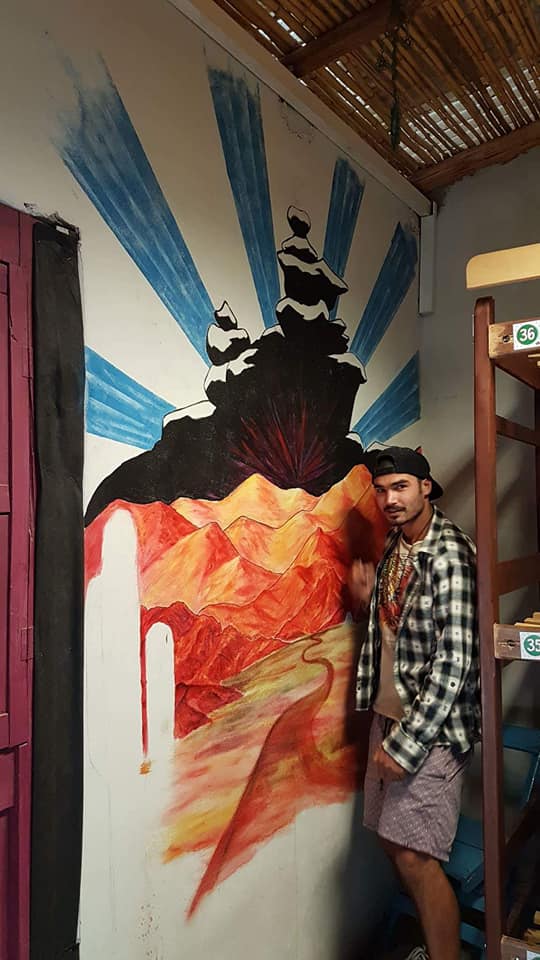 Artist beside a desert landscape mural with red rock formations and blue sun rays