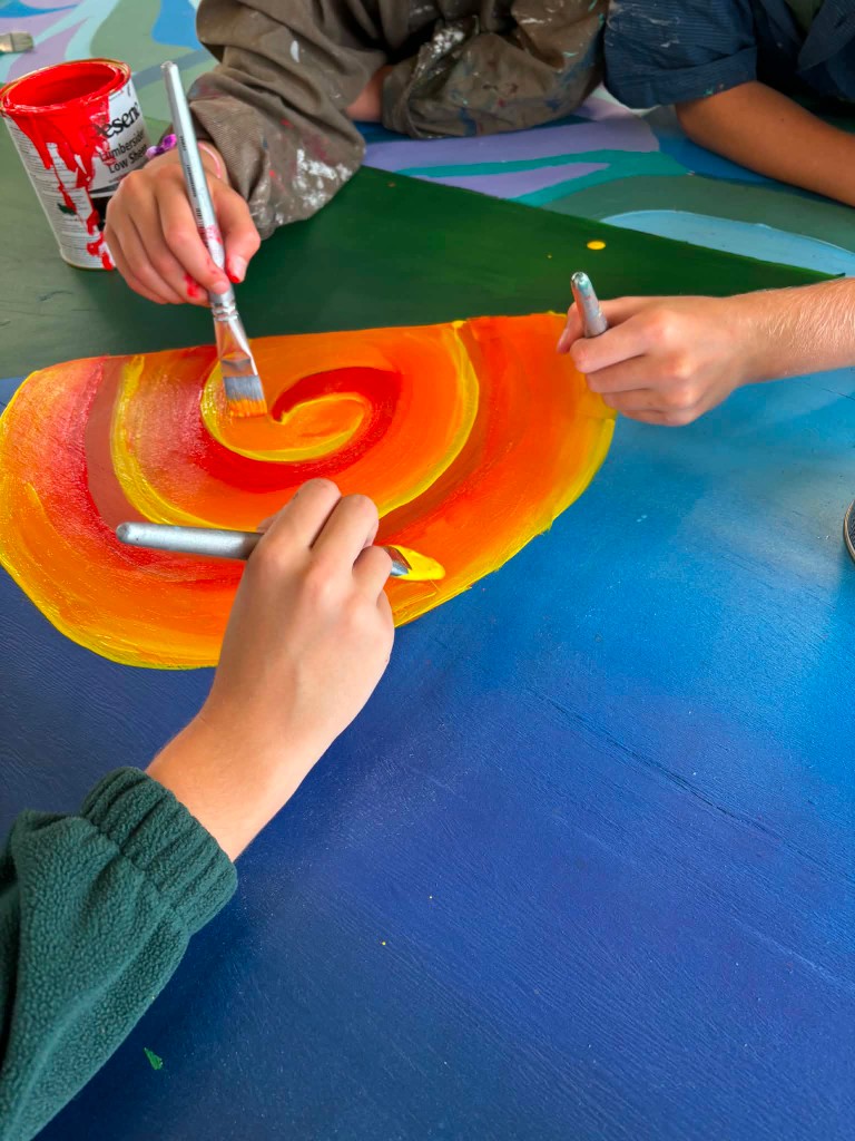 Children painting a colorful collaborative swirl mural together with brushes
