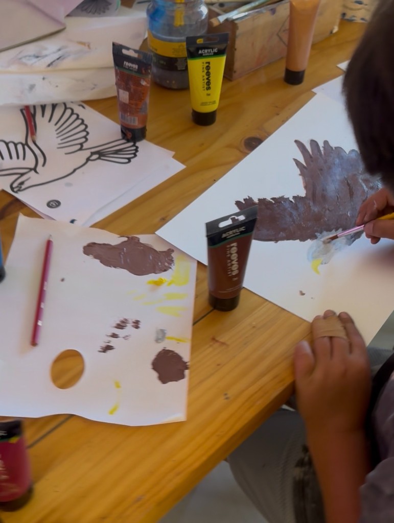 Child painting an eagle with acrylics at a workshop table