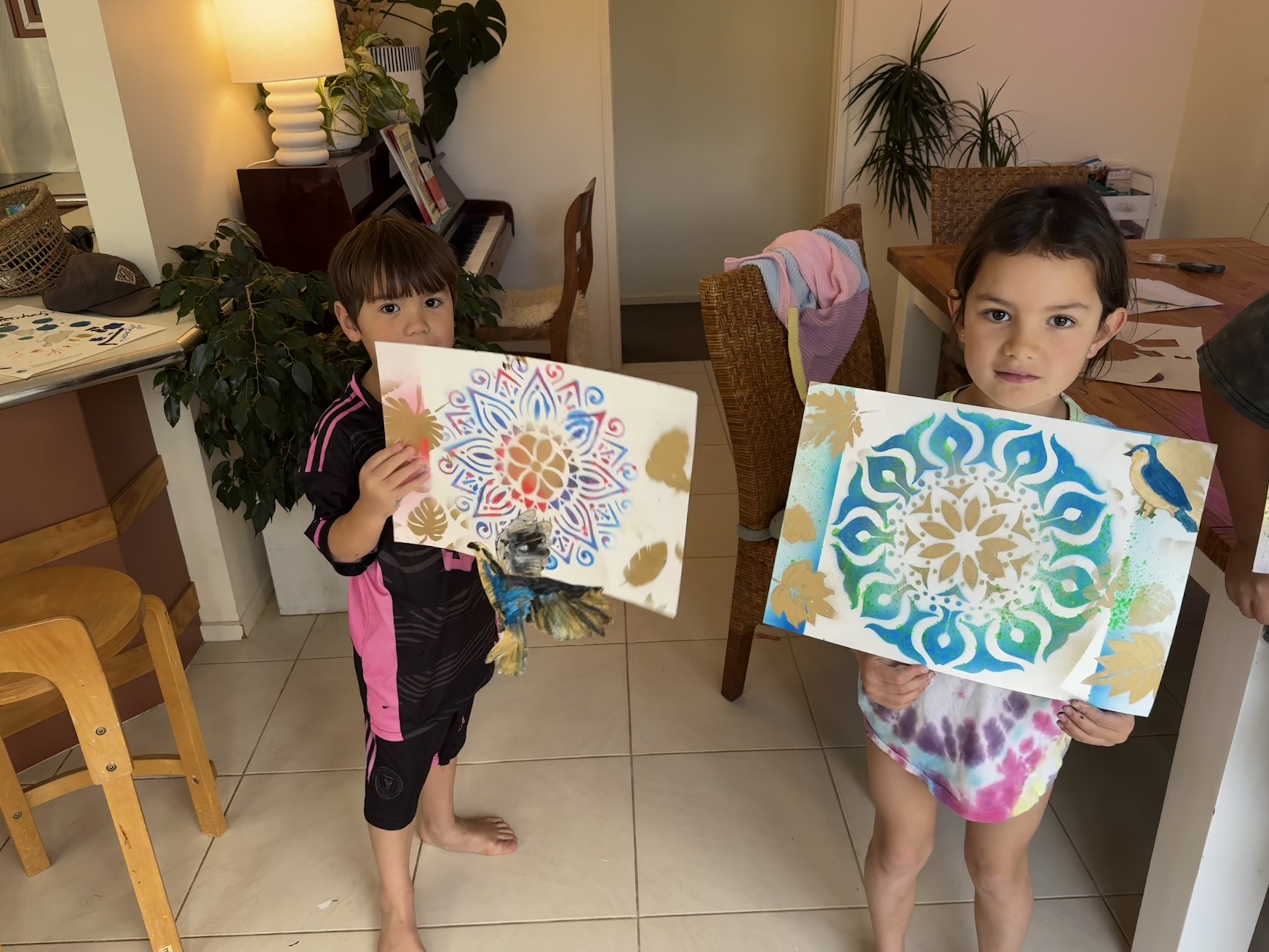 Two children holding up colourful mandala artwork at home