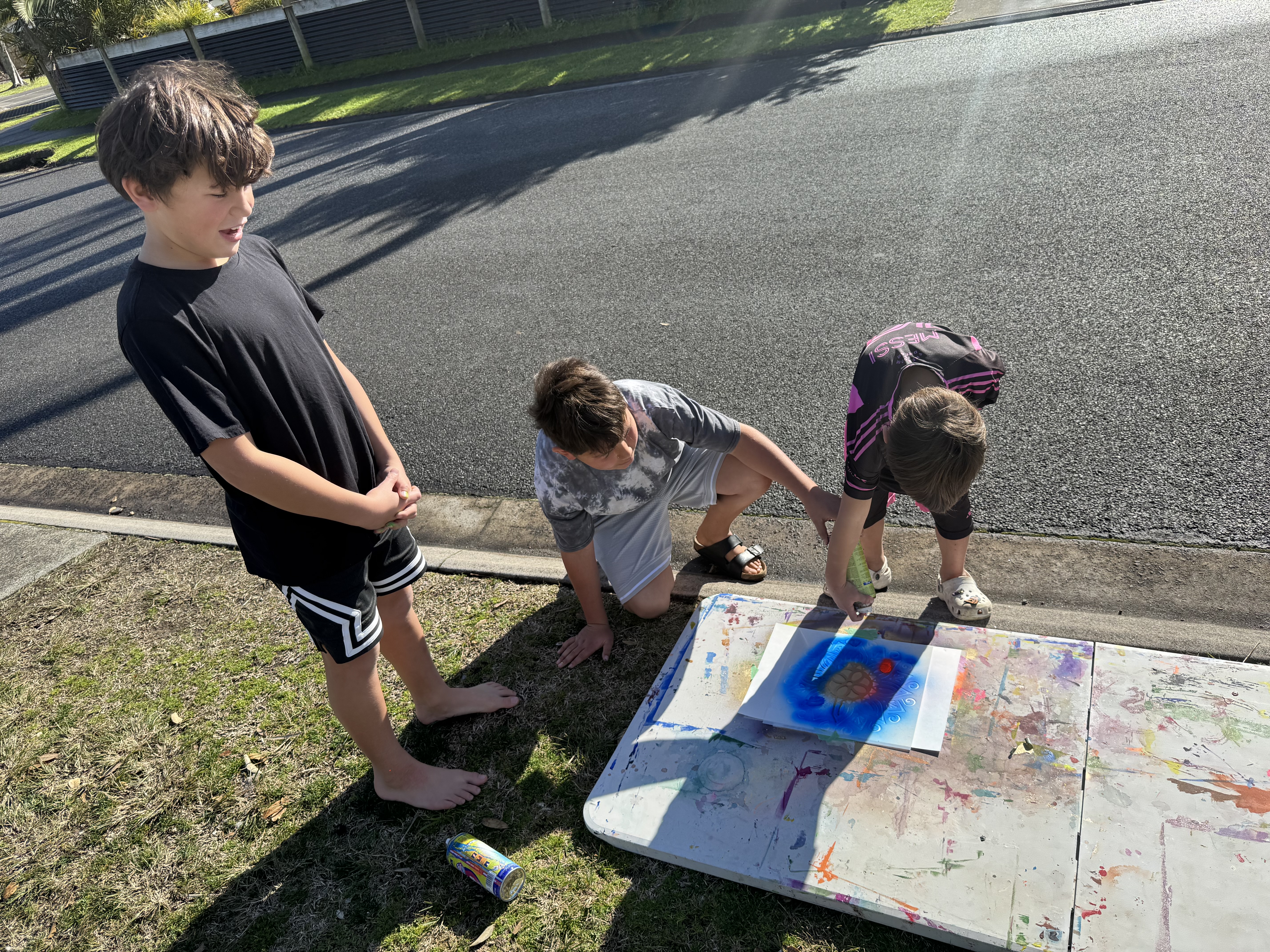 Three boys spray painting together at an outdoor workshop table