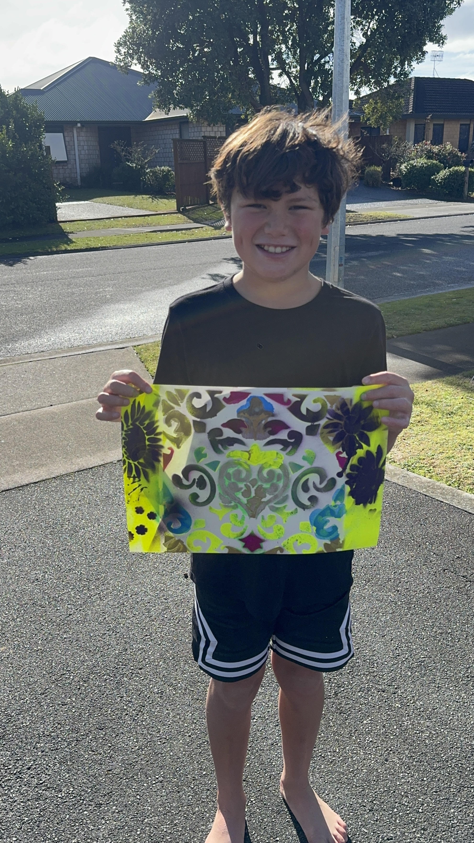 Boy holding up bright yellow stencil artwork outdoors