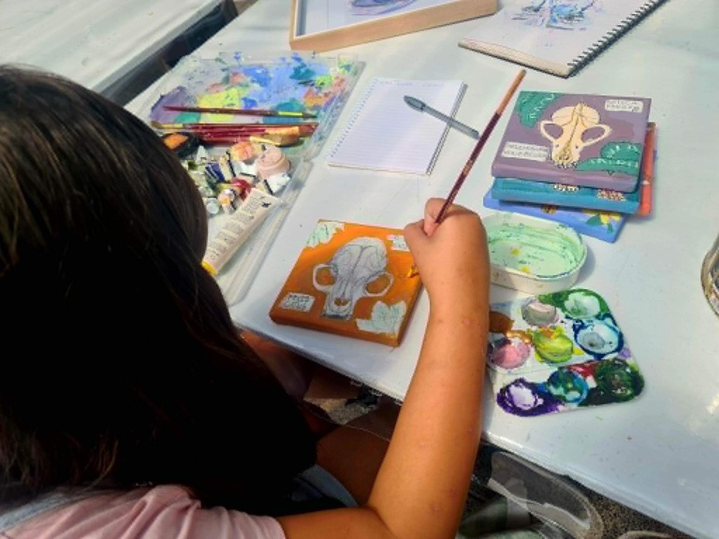Artist painting a colorful skull design on a small canvas at a table of art supplies