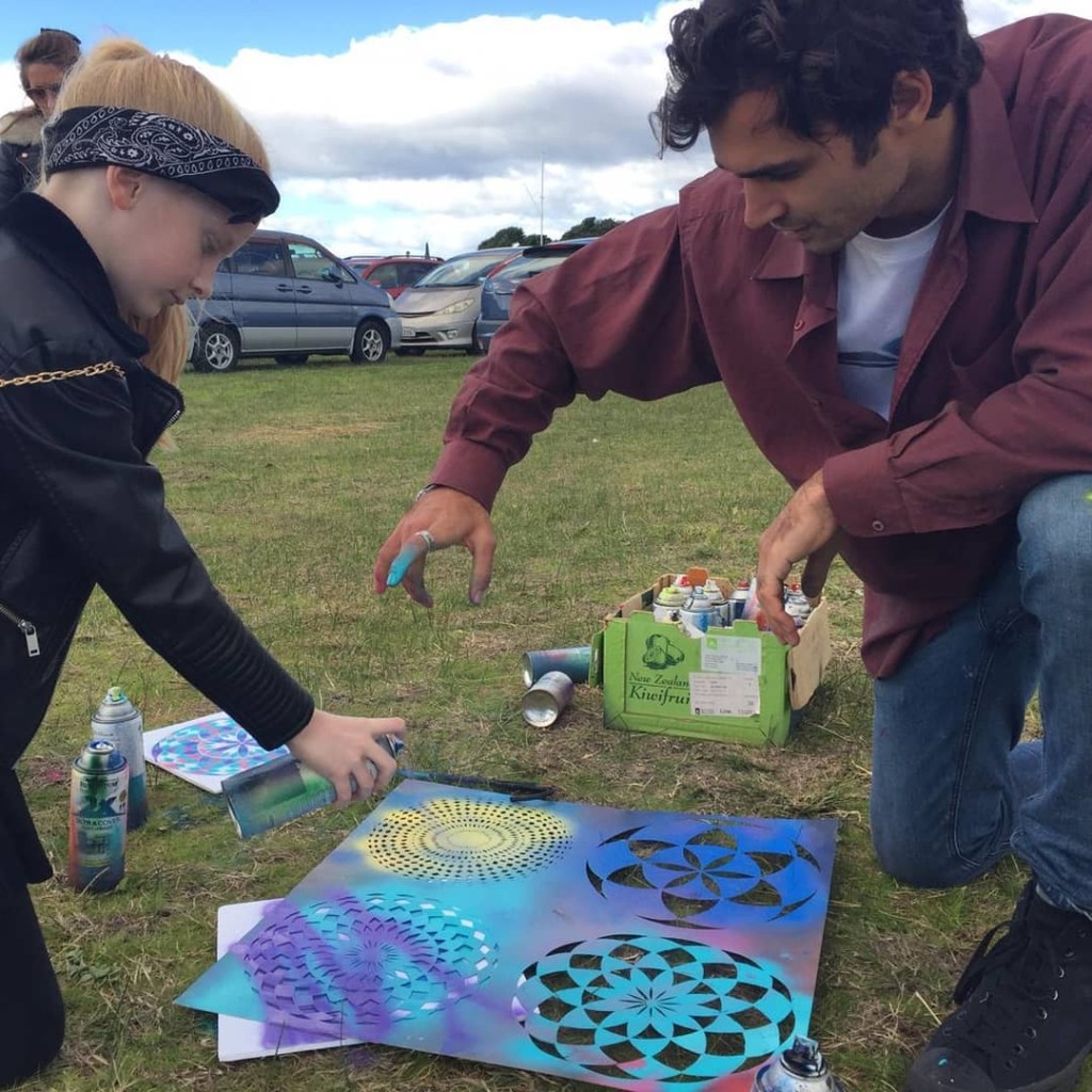 Facilitator and child collaborating on spray-paint stencil art during an outdoor workshop
