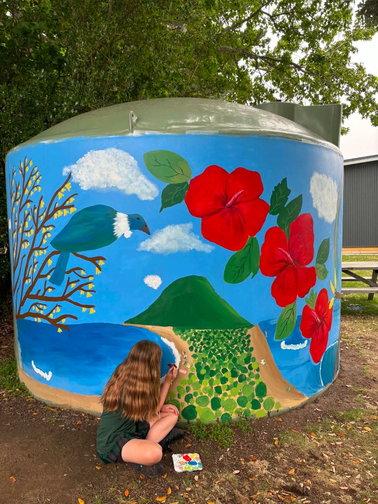 Girl painting a colorful nature mural on a large outdoor water tank