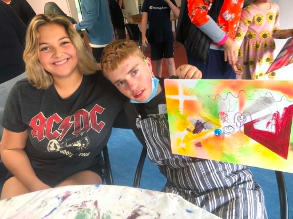 Two young people smiling and holding up a colorful abstract painting at a workshop