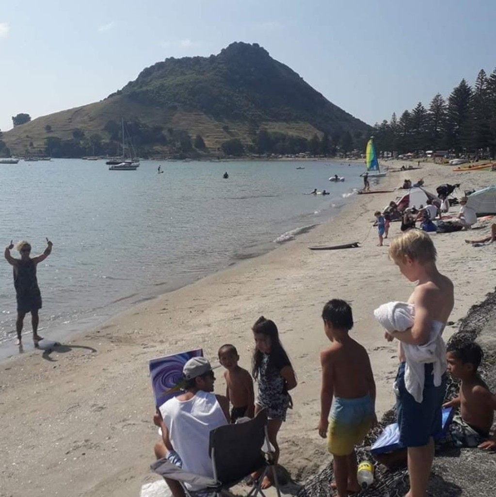 Artist painting outdoors on the beach with children watching during a plein air lesson
