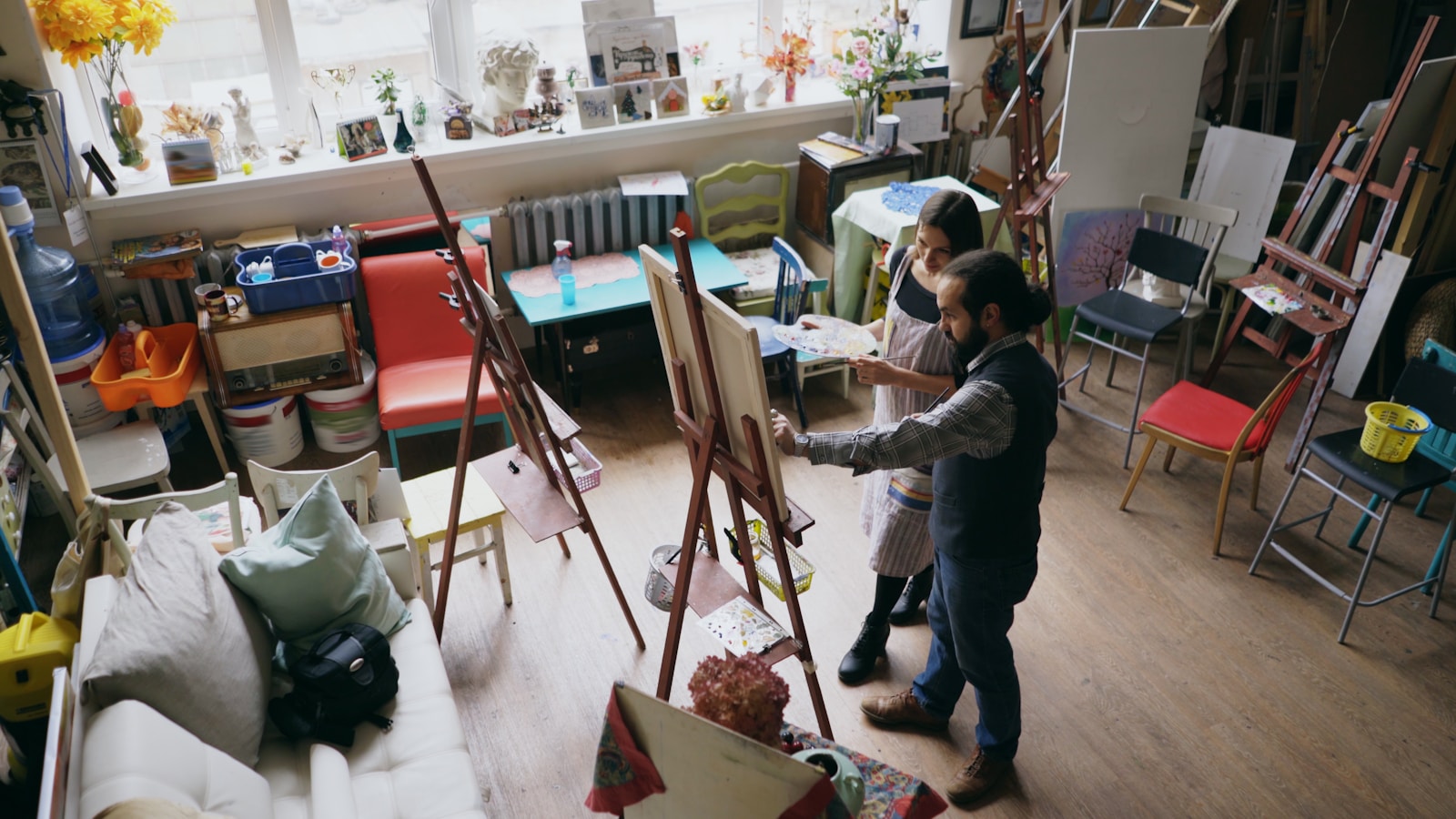 Instructor guiding a student painting on canvas in an art studio