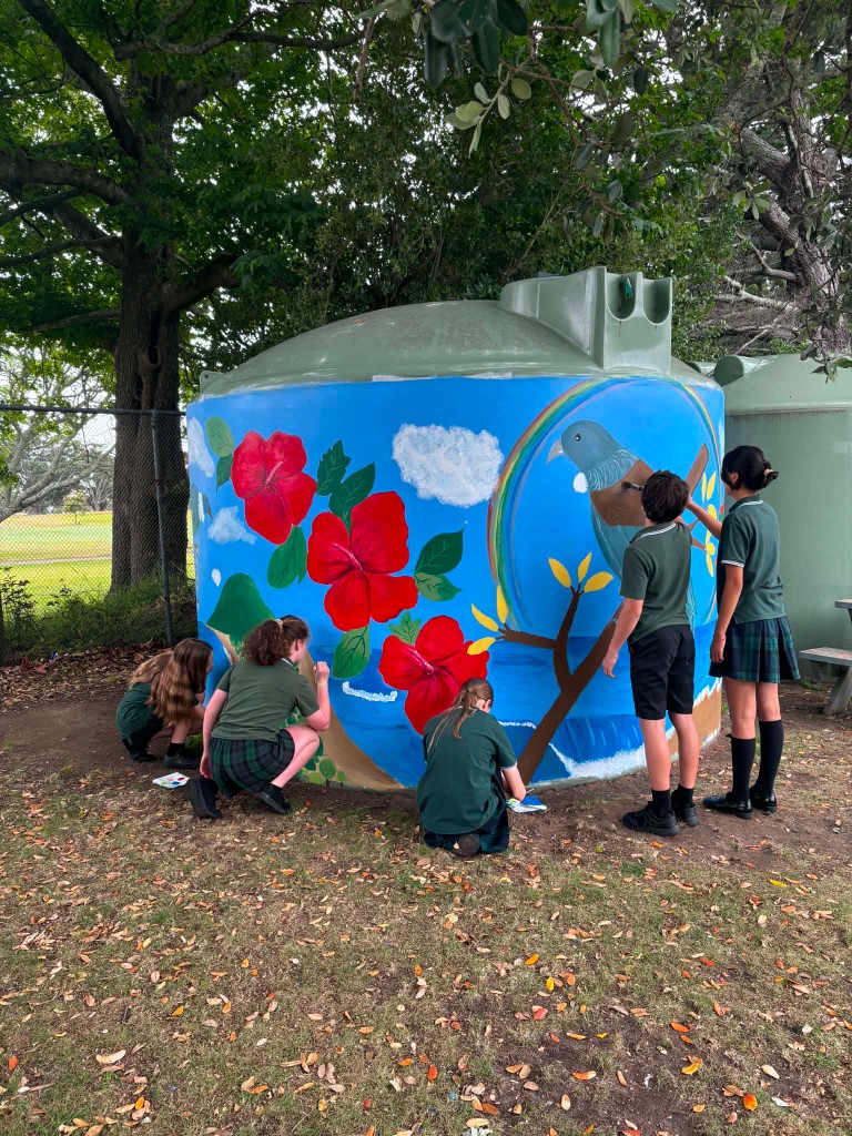 Students in school uniforms painting a colorful mural on a water tank