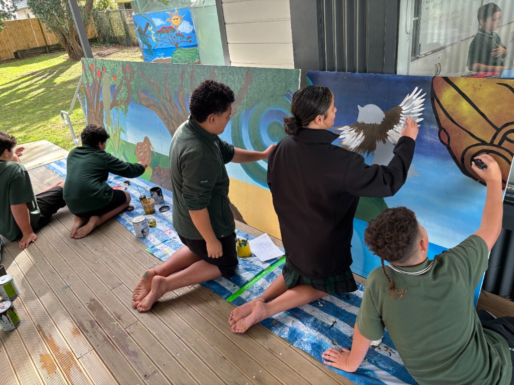 Students in school uniforms painting a Māori-themed mural on a deck